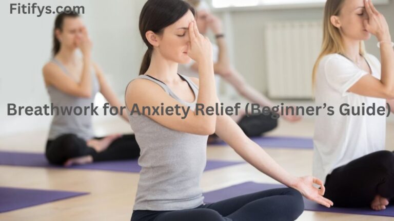 An image depicting a yoga class with several people in a seated meditation pose on purple mats. The person in the foreground, in a grey tank top and black leggings, has their right hand pinching their nostrils, likely performing Nadi Shodhana breathwork. The title of the image is "Breathwork for Anxiety Relief (Beginner's Guide)" and "Fitifys.com" is in the top left corner. The overall image suggests physical relaxation techniques.