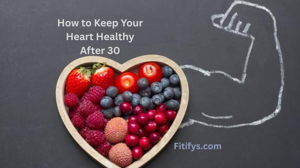 A heart-shaped wooden bowl filled with vibrant berries and fruits including strawberries, blueberries, raspberries, cherries, lychees, and tomatoes, placed on a blackboard surface. A chalk drawing of a muscular arm flexing is seen behind the bowl. The text reads “How to Keep Your Heart Healthy After 30” and “Fitifys.com.”