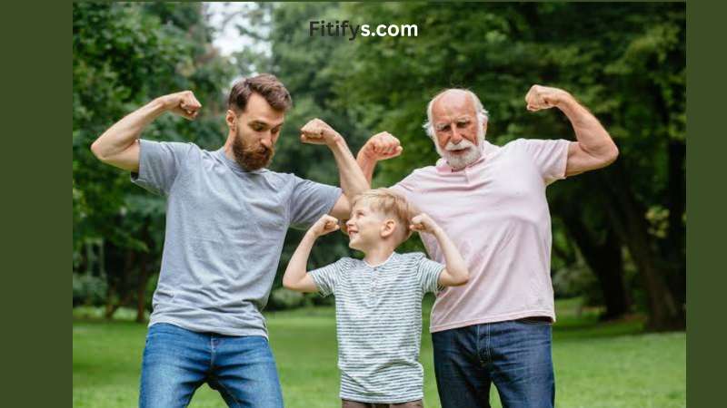 Three generations of males—grandfather, father, and young son—standing outdoors in a park, flexing their arm muscles and smiling at each other. The background is filled with green trees and grass, creating a lively and playful atmosphere. Text at the top reads "Fitifys.com."
